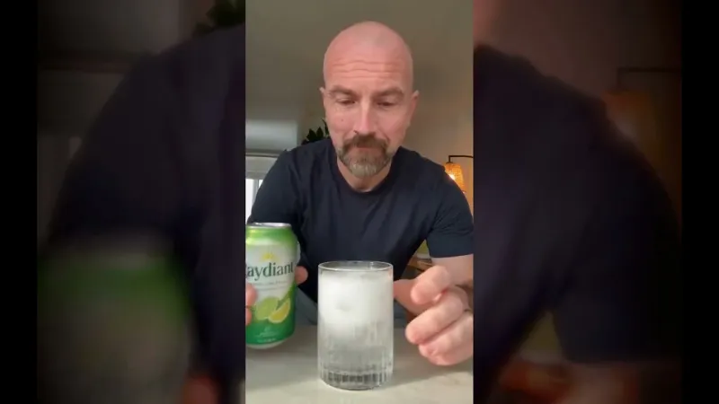 Ray at a kitchen counter holding a green Raydiant soda can beside a glass of ice, a frame from a generated commercial.